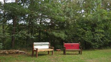 Zwei Holzbanken in einer grünen Parklandschaft, im Hintergrund dichtes Baumbestand.