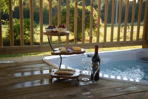A wooden deck with a hot tub, a three-tiered fruit and cheese board, and two glasses of wine.