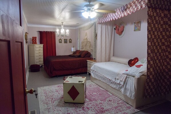 A bedroom with a bed, a dresser, a nightstand, a chandelier, and a ceiling fan.