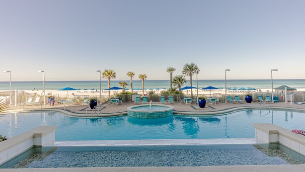 A pool area with a view of the beach, lounge chairs, and umbrellas.