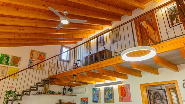 Un intérieur en bois à plusieurs niveaux, avec un escalier, des ventilateurs de plafond et des œuvres d’art accrochées aux murs.