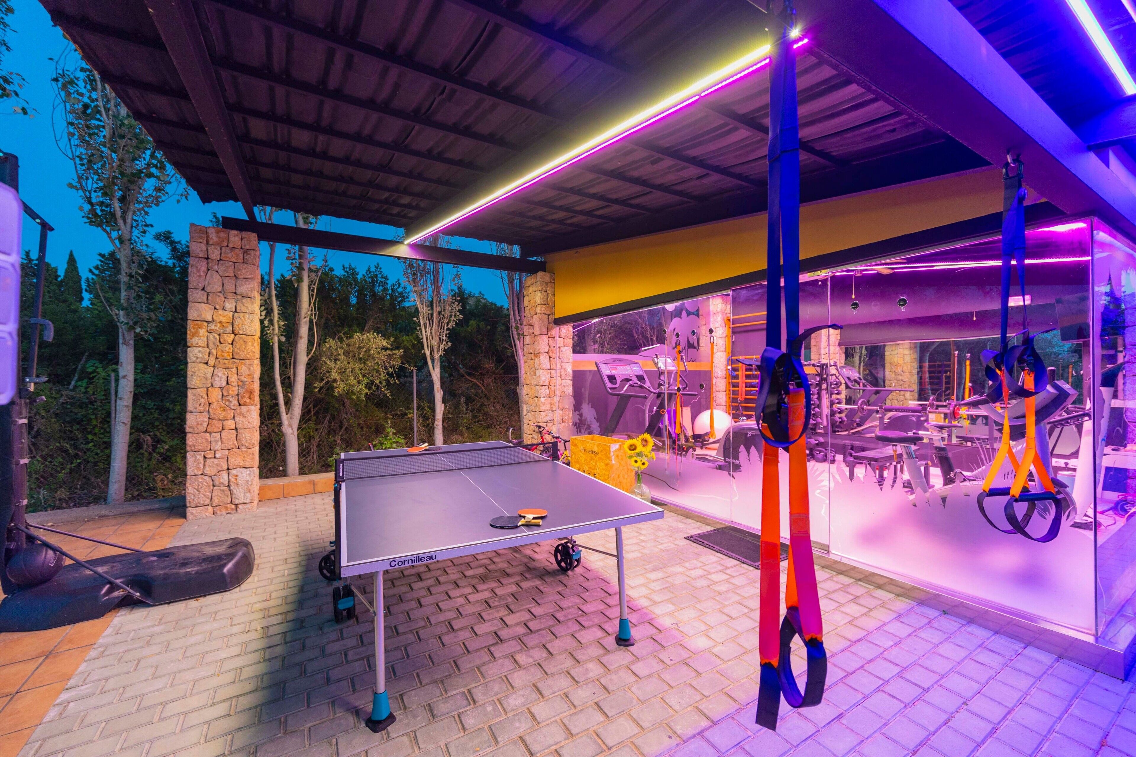 Een buitenterrein voor sport met een tafeltennistafel, fitnessapparatuur en een stenen muur.