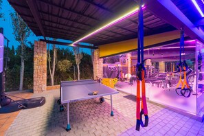 An outdoor sports area with a ping pong table, exercise equipment, and a stone wall.