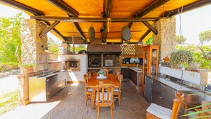 Un espace cuisine extérieur doté d’un sol en pierre, de meubles en bois et d’une variété d’ustensiles et d’appareils de cuisson.
