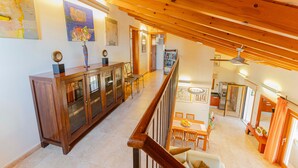 A spacious living area with a high ceiling, wooden beams, a dining table with chairs, a kitchen area, and a staircase leading to an upper level. - Country House 'Els Oscols 53' with Sea Views, Wi-Fi and Air Conditioning (Alcudia)