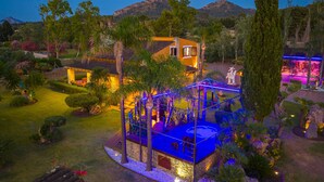 Un espace extérieur bien éclairé, doté d’une piscine, entouré d’une végétation luxuriante et avec une chaîne de montagnes en toile de fond.