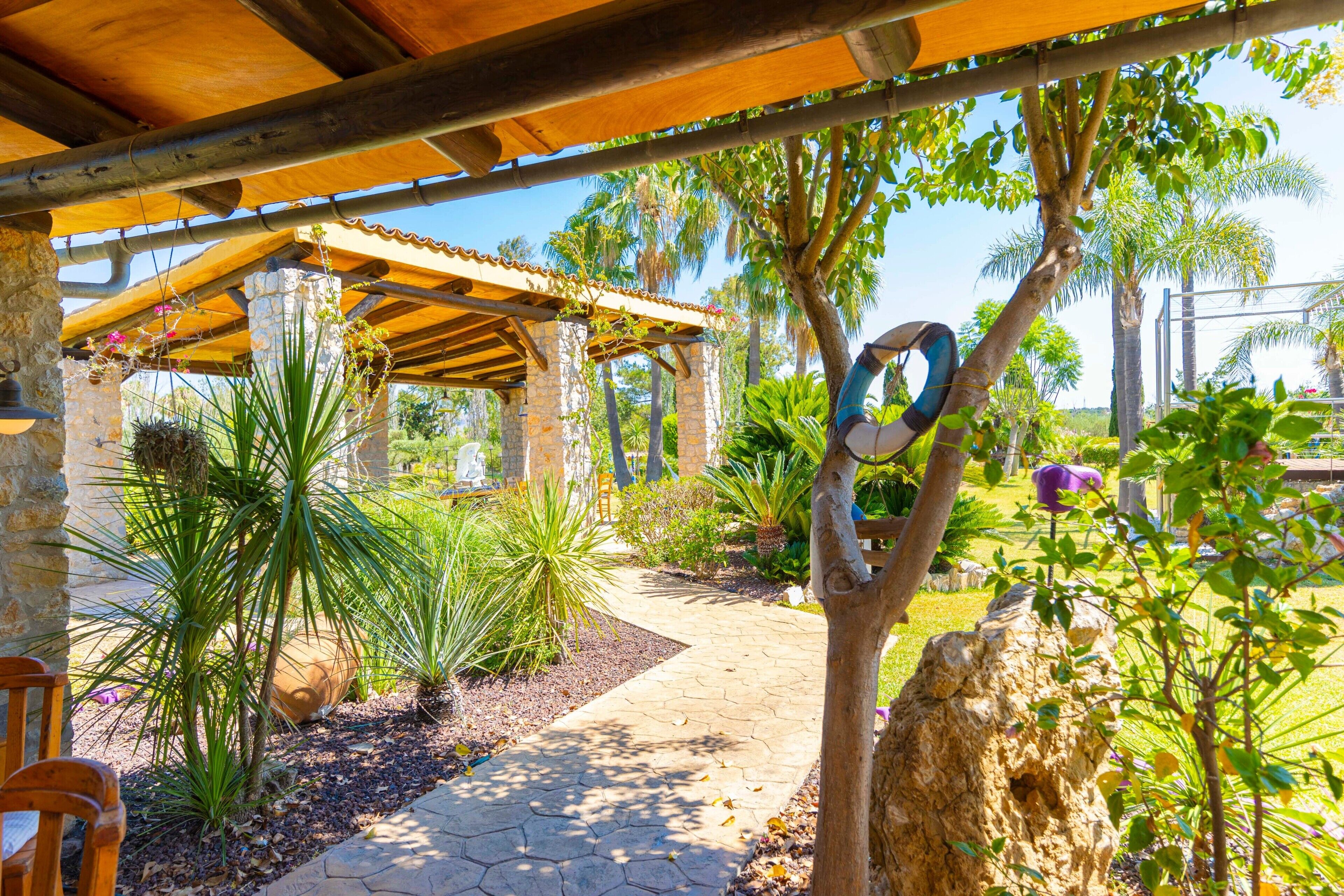 Un espace extérieur abrité, doté d’un mur en pierre, d’une pergola en bois et de diverses plantes.