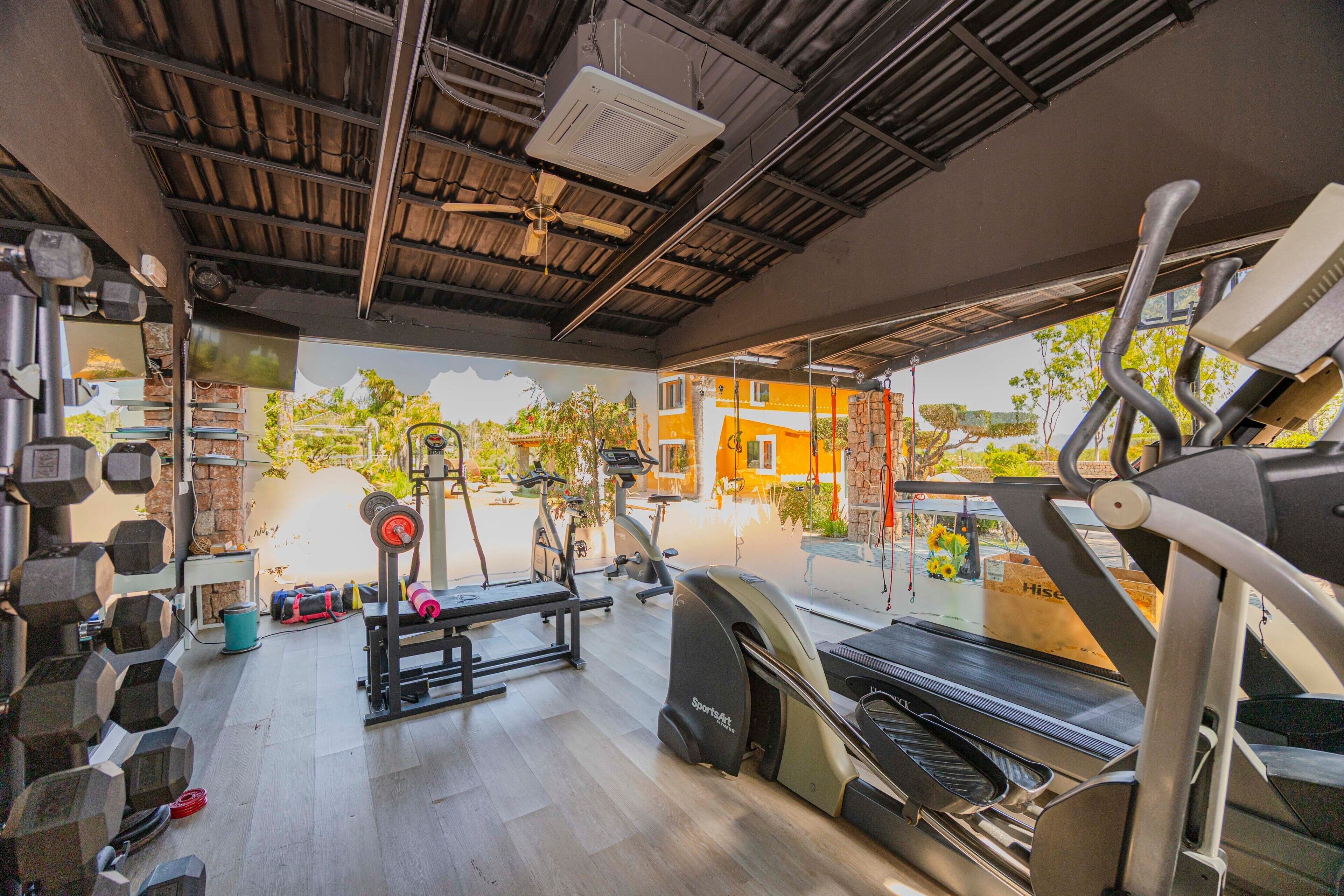 Et fitnesscenter med forskellig træningsudstyr, herunder håndvægte, en bænkpres og konditionsmaskiner.