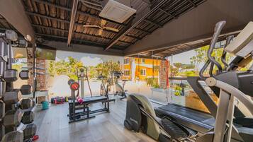 Ein Fitnessstudio mit unterschiedlichen Trainingsgeräten, darunter Kurzhanteln, eine Hantelbank und Cardiogeräte.
