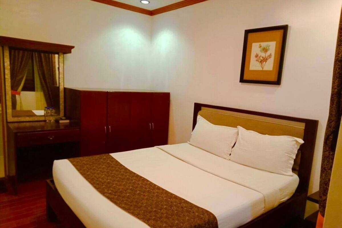 A hotel room with a bed, a desk, a wardrobe, and a framed picture on the wall.