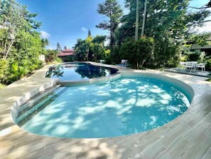 A swimming pool with a curved edge, surrounded by a wooden deck and lush greenery. - Hortz Hotels and Resorts (Tagaytay)