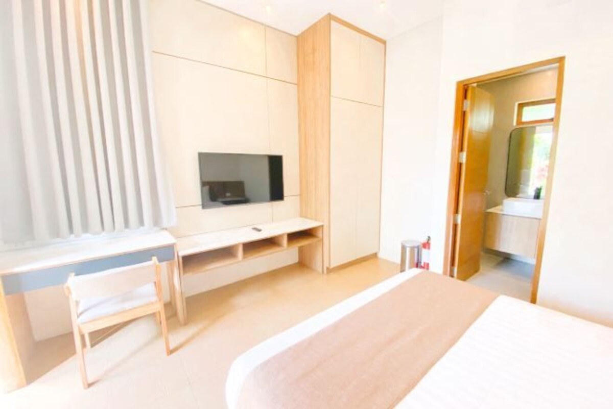 A modern bedroom with a bed, a desk, a chair, and a TV.
