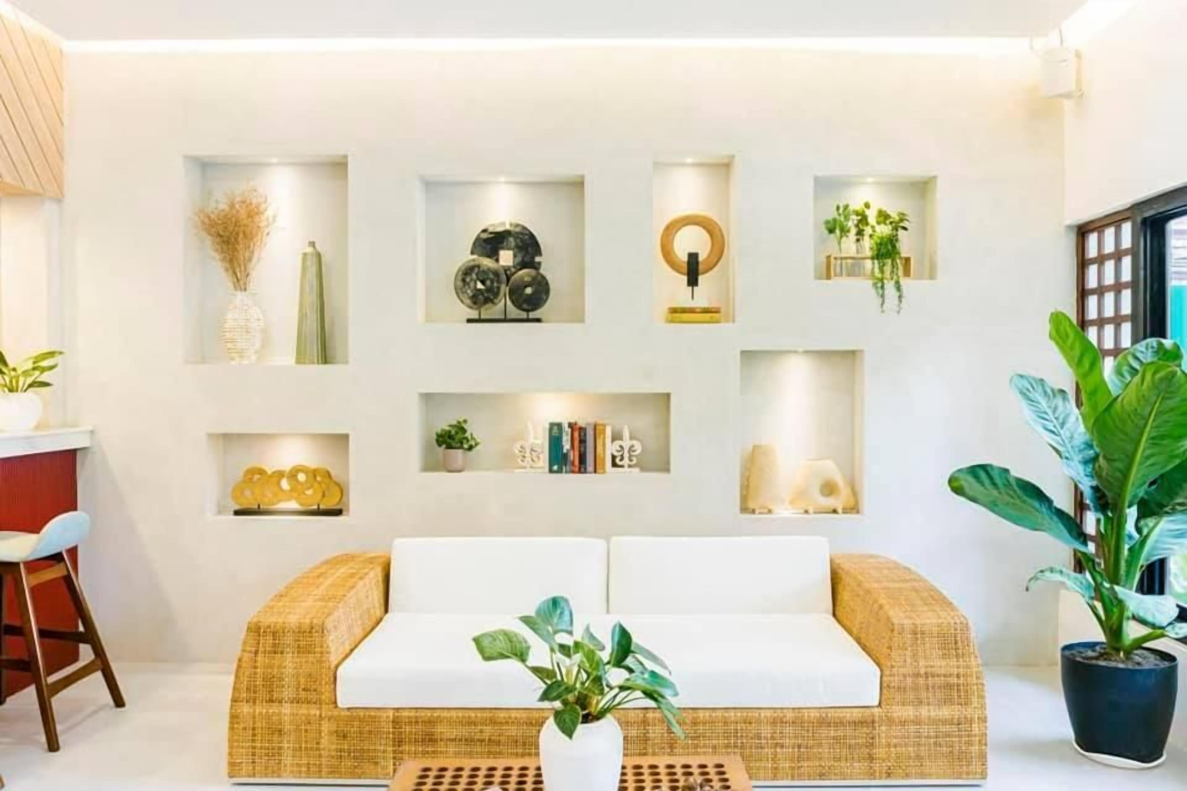 A modern living room with a wicker sofa, a coffee table, and a variety of decorative items on shelves.