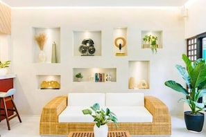 A modern living room with a wicker sofa, a coffee table, and a variety of decorative items on shelves. - Hortz Hotels and Resorts (Tagaytay)
