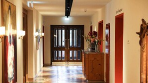 Un corridoio d'hotel con pavimento piastrellato, porte in legno e una reception con un vaso di fiori.