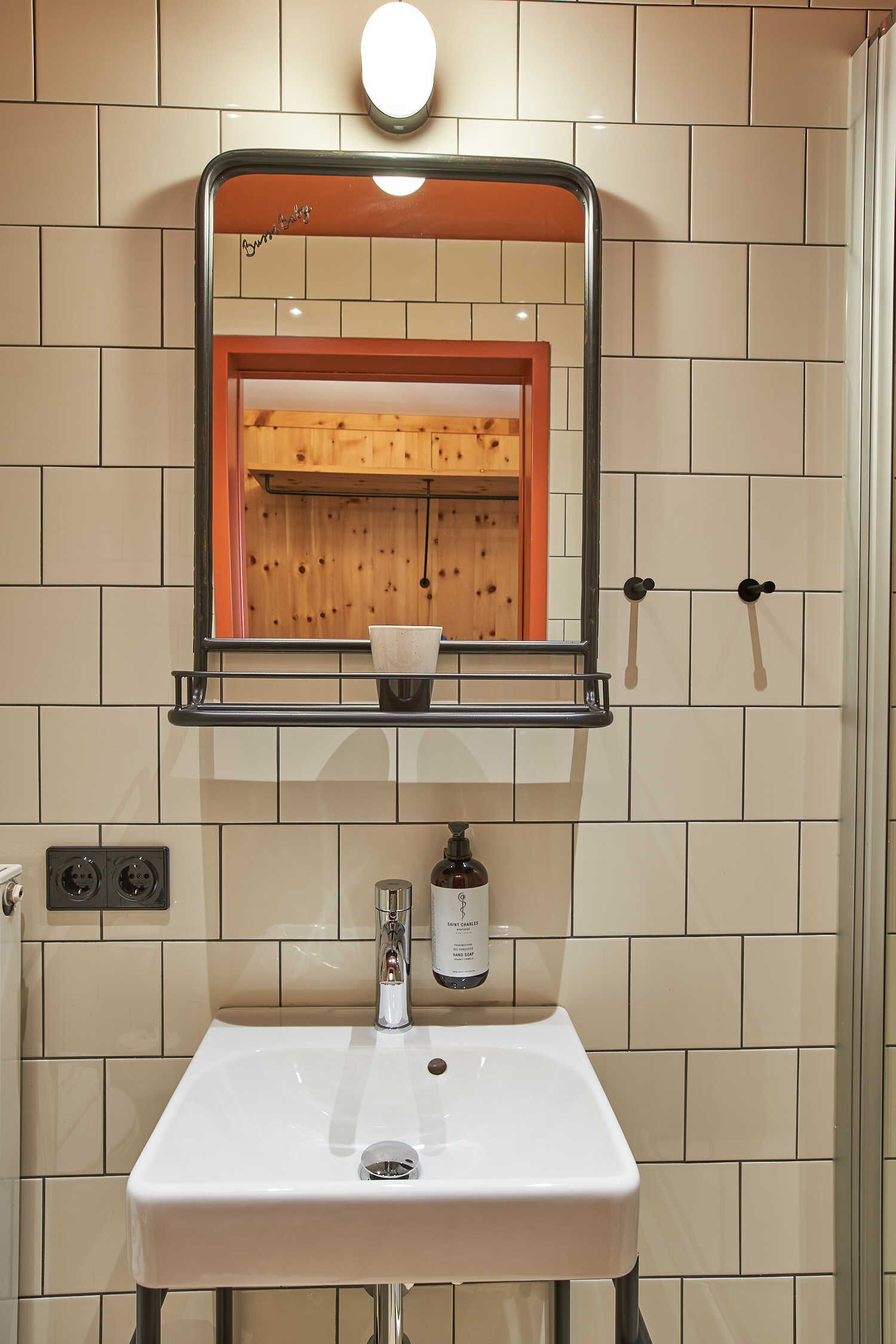 A bathroom with a white sink, a mirror with a wooden frame, and a shelf with a cup.