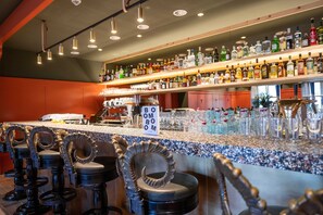 Un espace bar comprenant un comptoir, des tabourets et des étagères remplies de bouteilles et de verres.