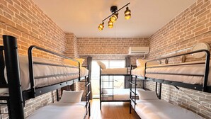 Une chambre d’auberge de jeunesse avec des lits superposés, des murs en briques, un plancher en bois et un luminaire au plafond.