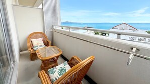 Un balcon agrémenté de meubles en osier, d’une table en verre et offrant une vue sur la mer et les bâtiments.