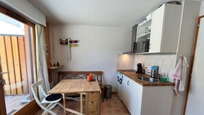 A compact kitchen with a wooden table, a bench, and a dog lying on the floor.