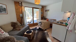 A cozy room with a sofa, a small wooden table, a bench, and a kitchen area with a sink and a window overlooking a snowy outdoor area.