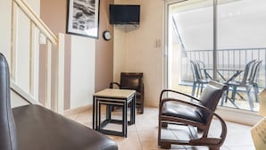 A modern living room with a sofa, a small table, a chair, a television, and a balcony with plastic chairs.