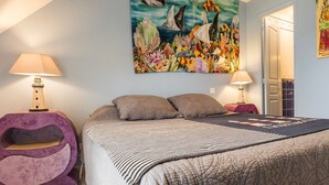 A bedroom with a bed, two bedside lamps, a painting, and a door.