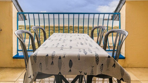 A balcony with a table and chairs, overlooking a beach.
