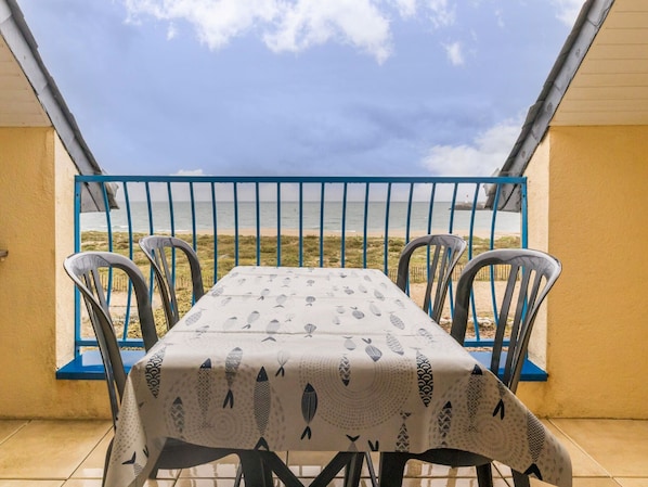 A balcony with a table and chairs, overlooking a beach.