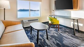 Hotelværelse med sofa, lille bord, stol, skrivebord, fladskærms-TV, vindue med udsigt over vandet og en aircondition.
