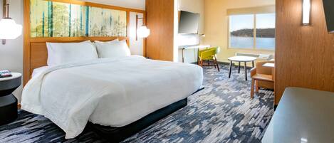 A hotel room with a large bed, a desk with a chair, a TV, and a view of the water.