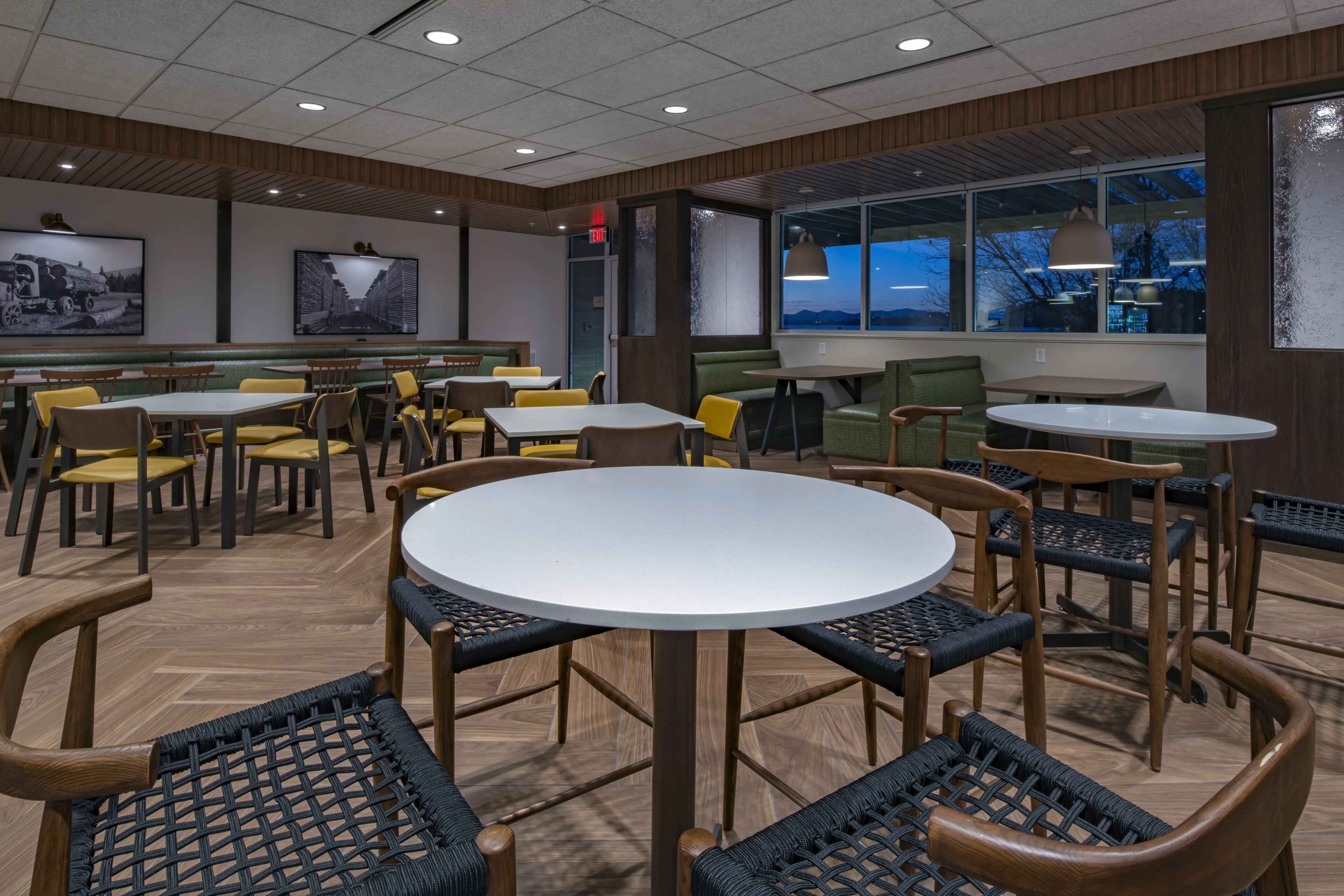 Un espace de restauration moderne avec des tables et des chaises rondes, des panneaux de bois et des œuvres d’art accrochées aux murs.