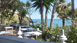 An outdoor seating area with white tables and chairs, surrounded by palm trees and a view of the ocean. - Hill Collection 5 apt, only 1km from Carvajal beach. In Higueron urbanisation (Fuengirola)
