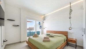 A modern bedroom with a large bed, a wooden headboard, and a view of the city through a sliding glass door. - Hill Collection 5 apt, only 1km from Carvajal beach. In Higueron urbanisation (Fuengirola)