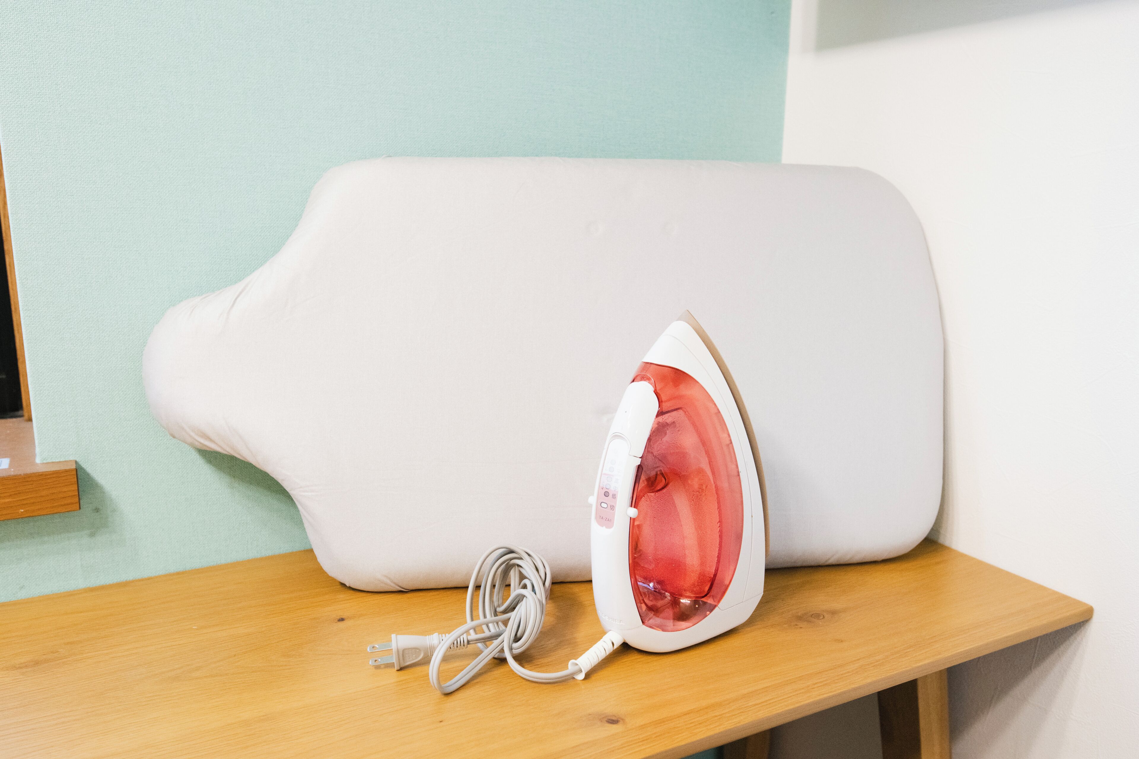 A white iron with a red heating element on a wooden table against a teal wall.