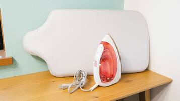 A white iron with a red heating element on a wooden table against a teal wall.