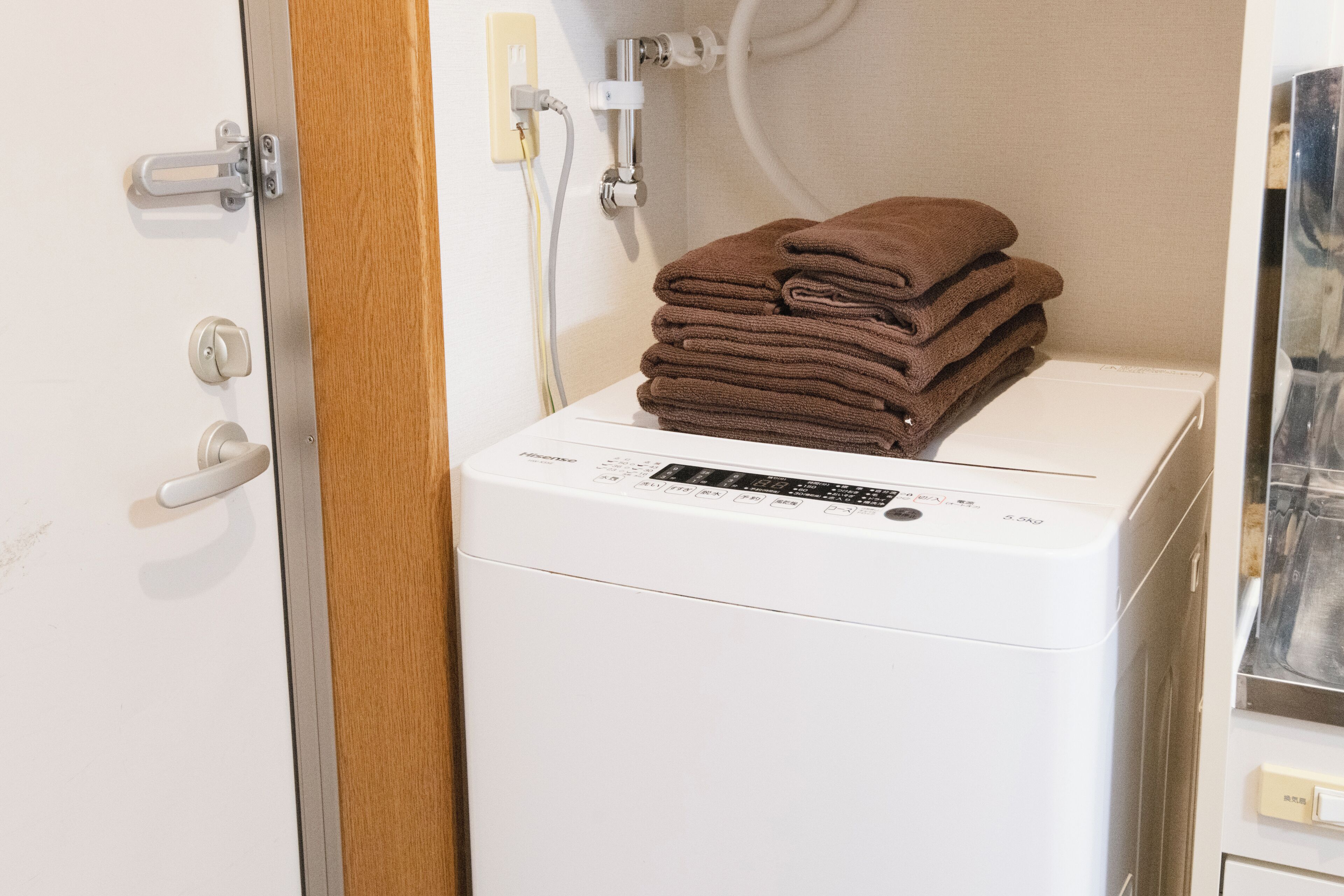 Una lavadora blanca con un panel de control, una puerta de madera y una pila de toallas encima.
