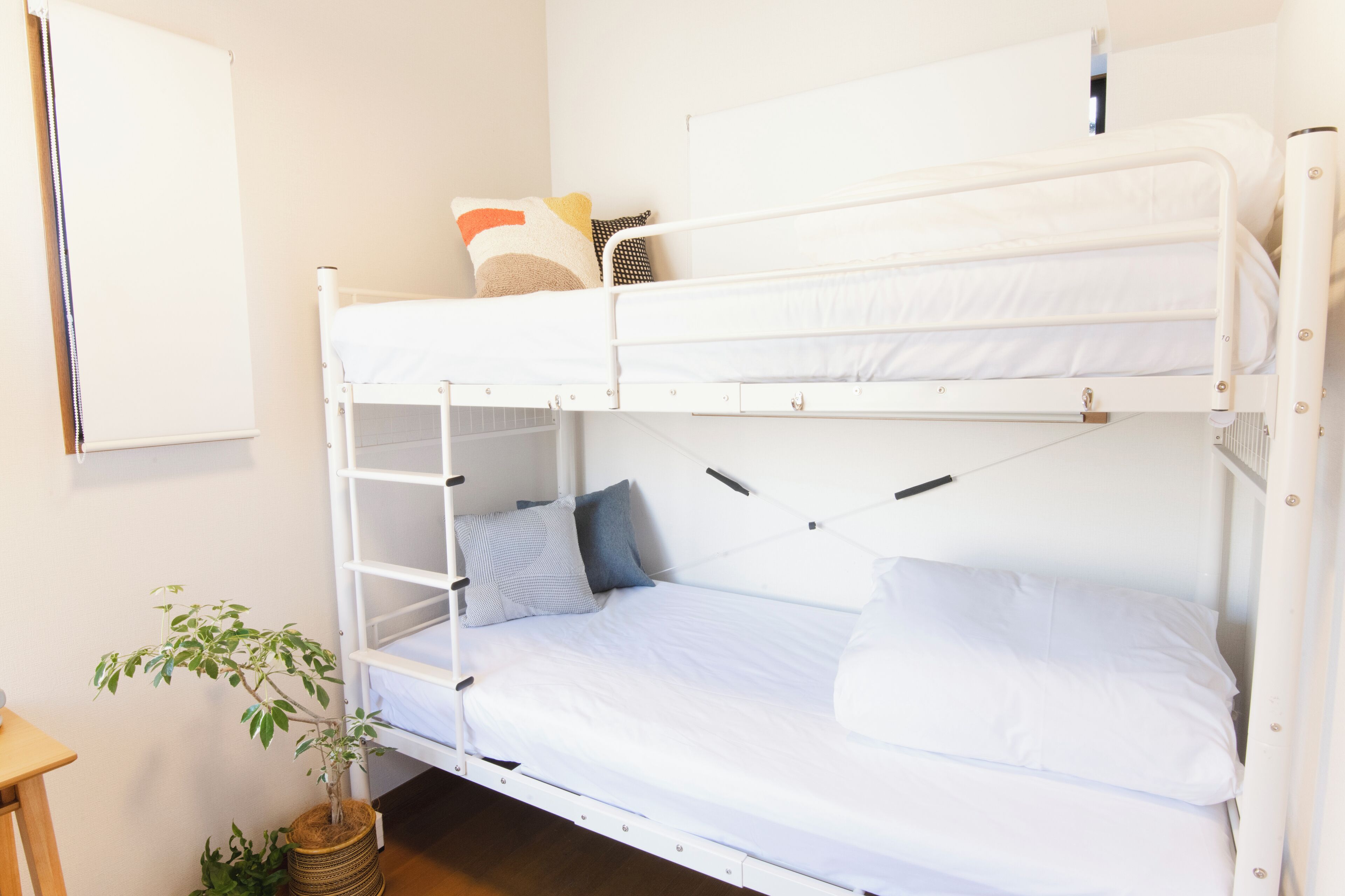 A bunk bed with white bedding and pillows, a small plant, and a wooden stool.