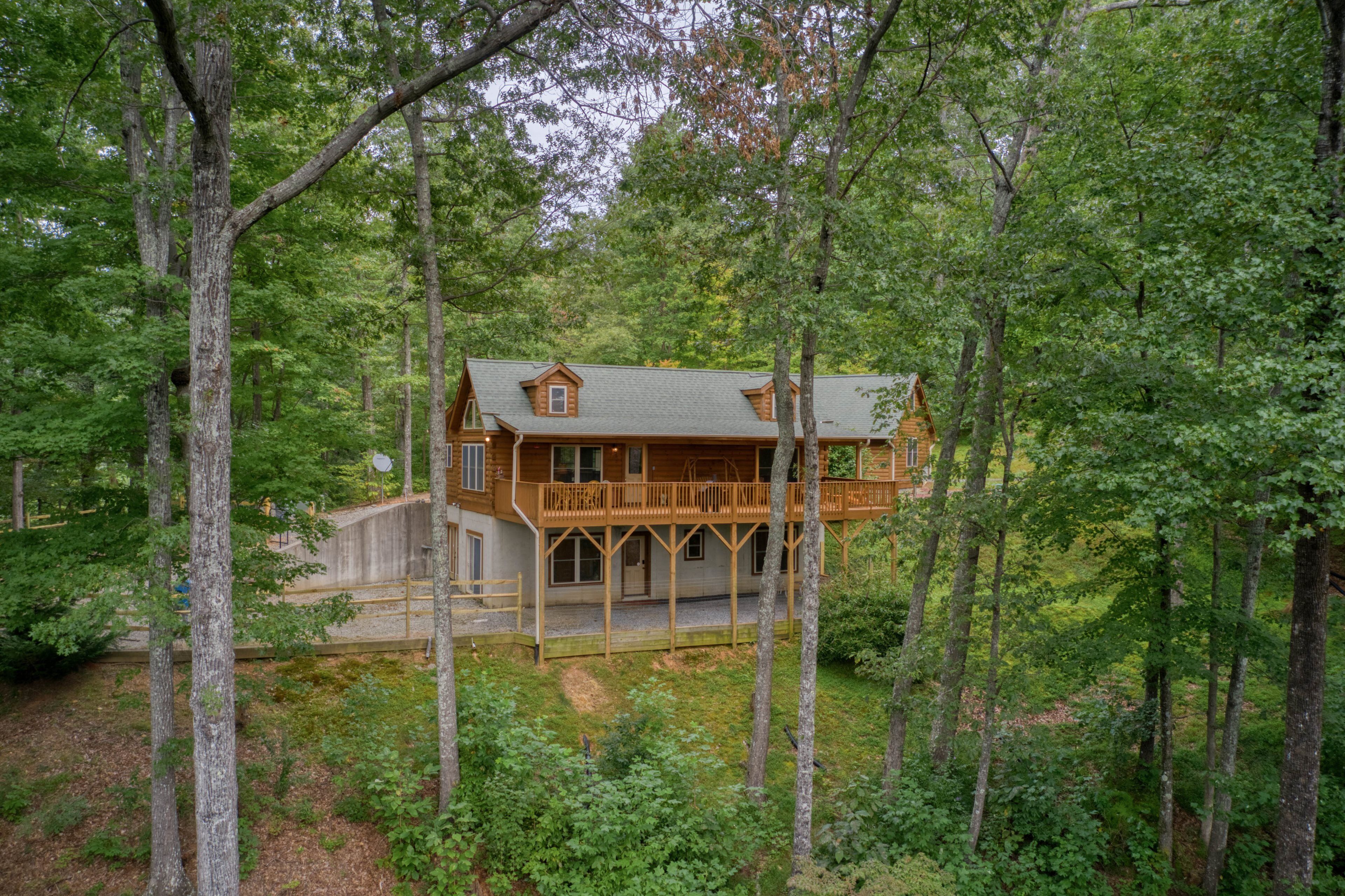 A cabin with a wooden deck and a covered porch, surrounded by dense forest.