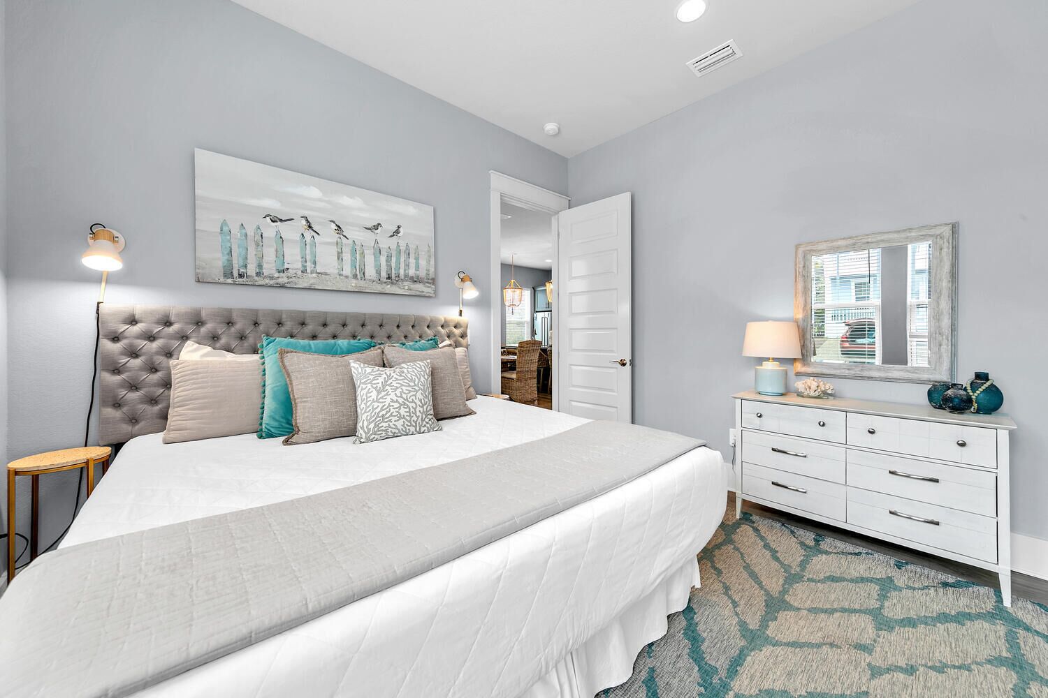Une chambre à coucher avec une tête de lit capitonnée, un lit blanc, une commode et un miroir.