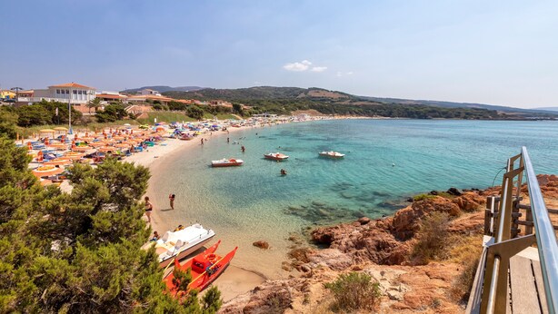 A beach with clear water, boats, and umbrellas.