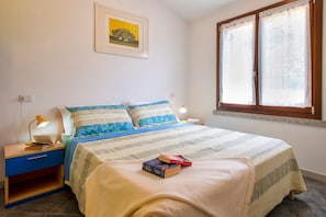 Une chambre à coucher avec un lit, des tables de chevet, une lampe, un tableau encadré au mur et une fenêtre avec des rideaux.