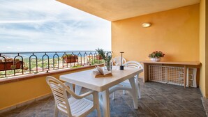 A balcony with a table, chairs, a potted plant, and a view of the sea.