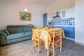 Un salon avec un canapé, une table à manger avec des chaises, un coin cuisine avec des placards et un sol carrelé.
