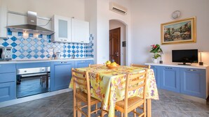 A kitchen with blue cabinets, a dining table with a floral tablecloth, and a television on a stand.