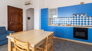 A compact kitchen with blue cabinets, a wooden dining table, and a blue sofa.