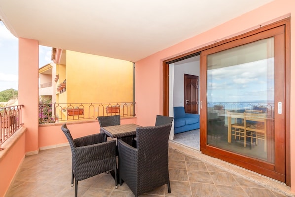 A balcony with a table and chairs, a sliding glass door, and a view of a building in the background.