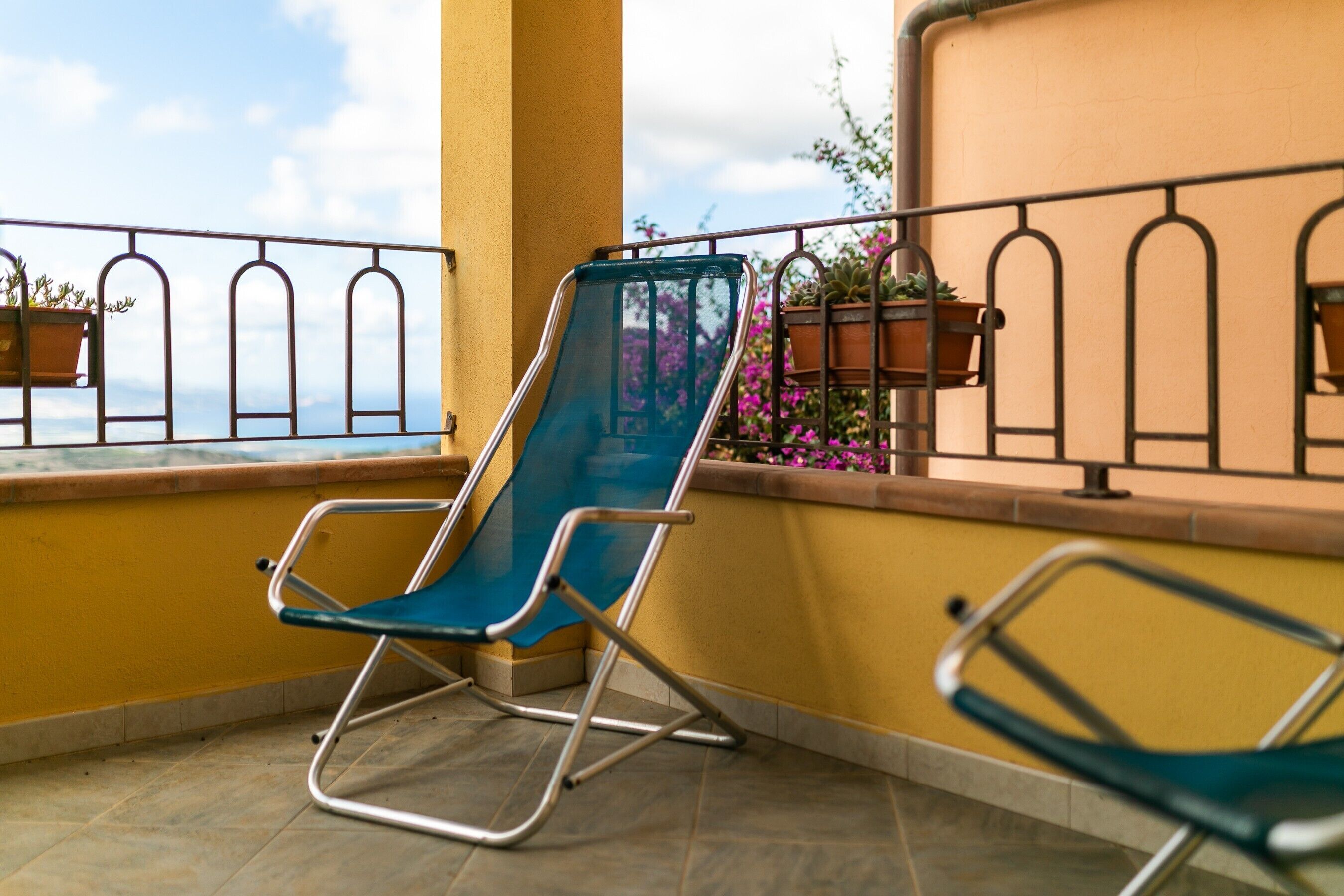 Un balcon avec une chaise bleue, une deuxième chaise et des plantes en pot.