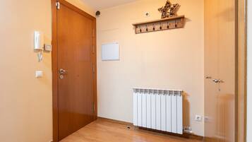 A room with a wooden door, a white radiator, a whiteboard, and a shelf with hooks.