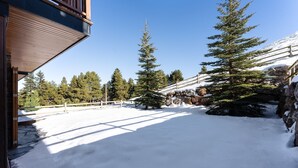 Un espace extérieur enneigé, doté d’une terrasse en bois, d’un mur en pierre et d’arbres à feuilles persistantes.
